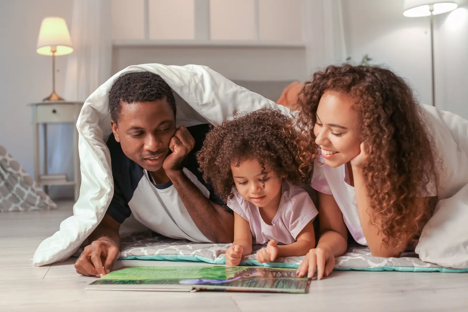 Família deitada no chão lendo junto, em casa com a TIM UltraFibra é boa para streaming e estudo