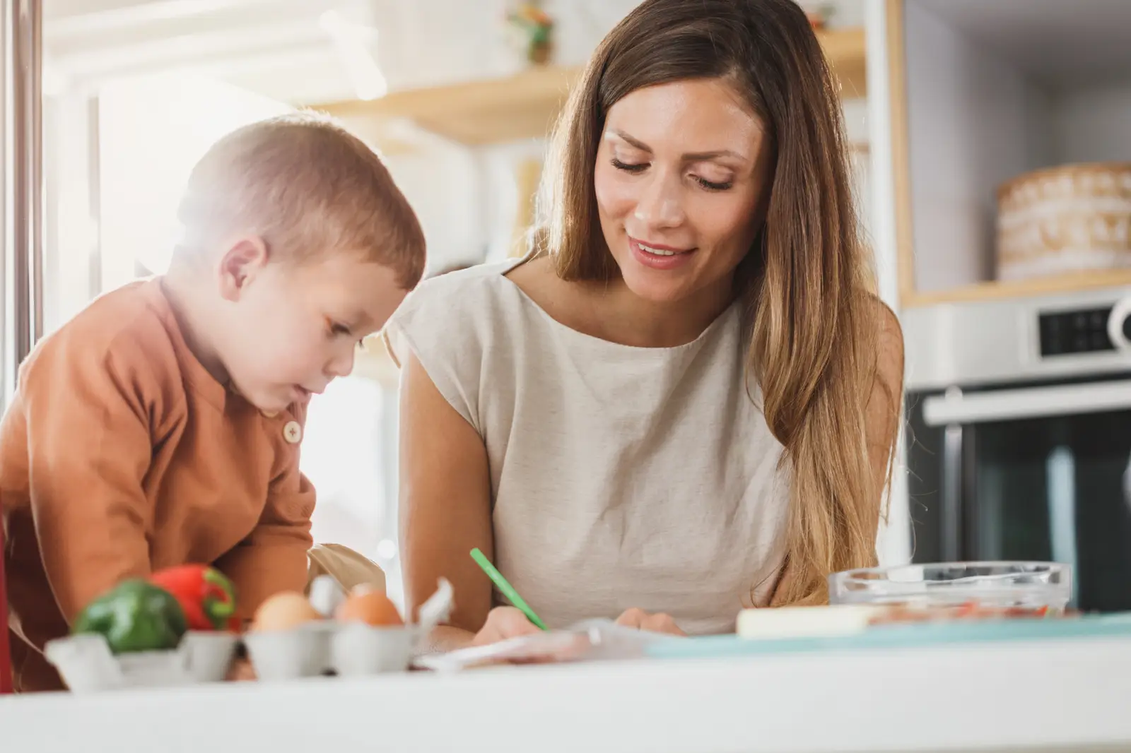 Mãe ajudando o filho com a lição na mesa de casa, com internet para estudar