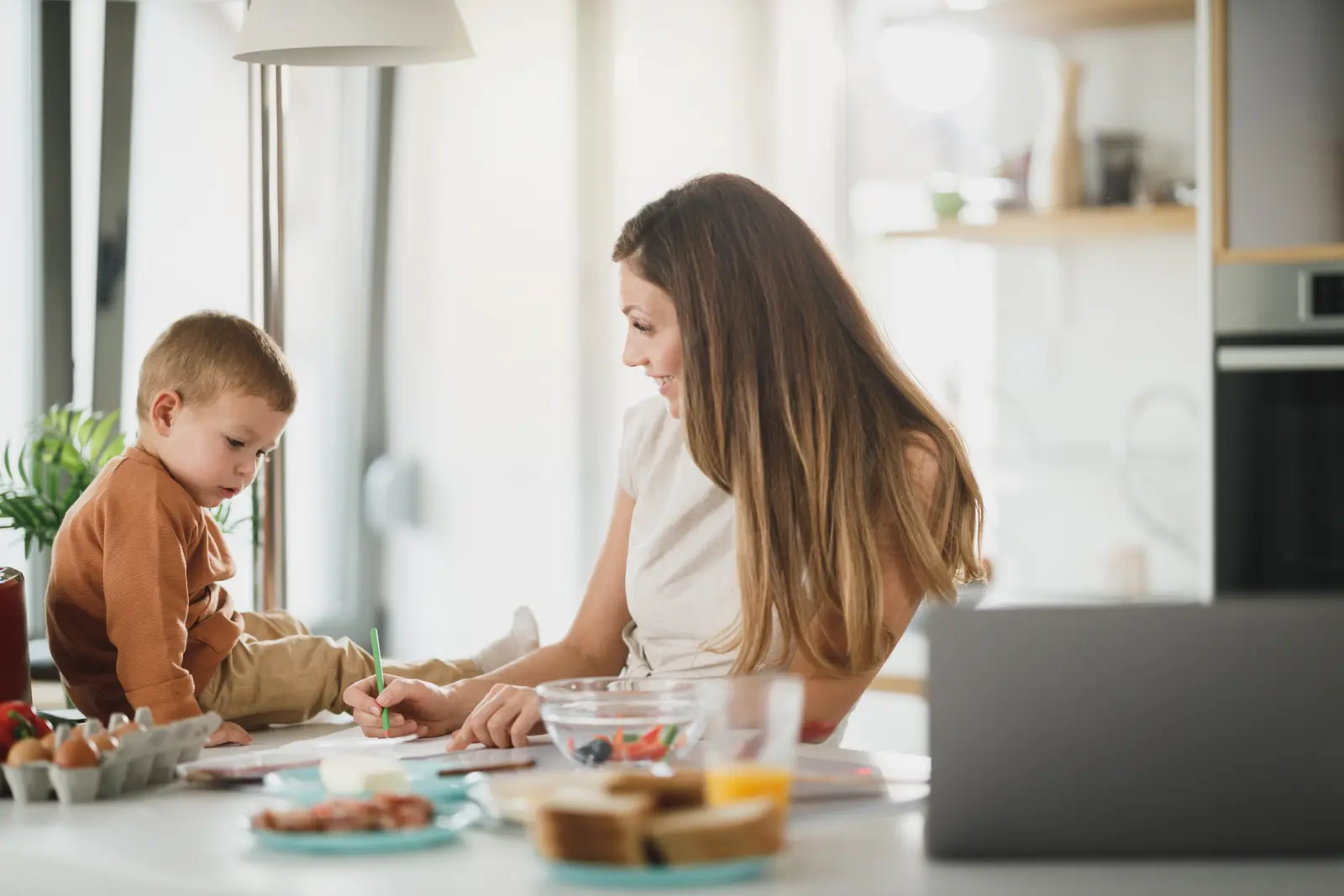 Mãe e filho usando notebook na cozinha, longe do roteador, com Wi-Fi de roteador mesh